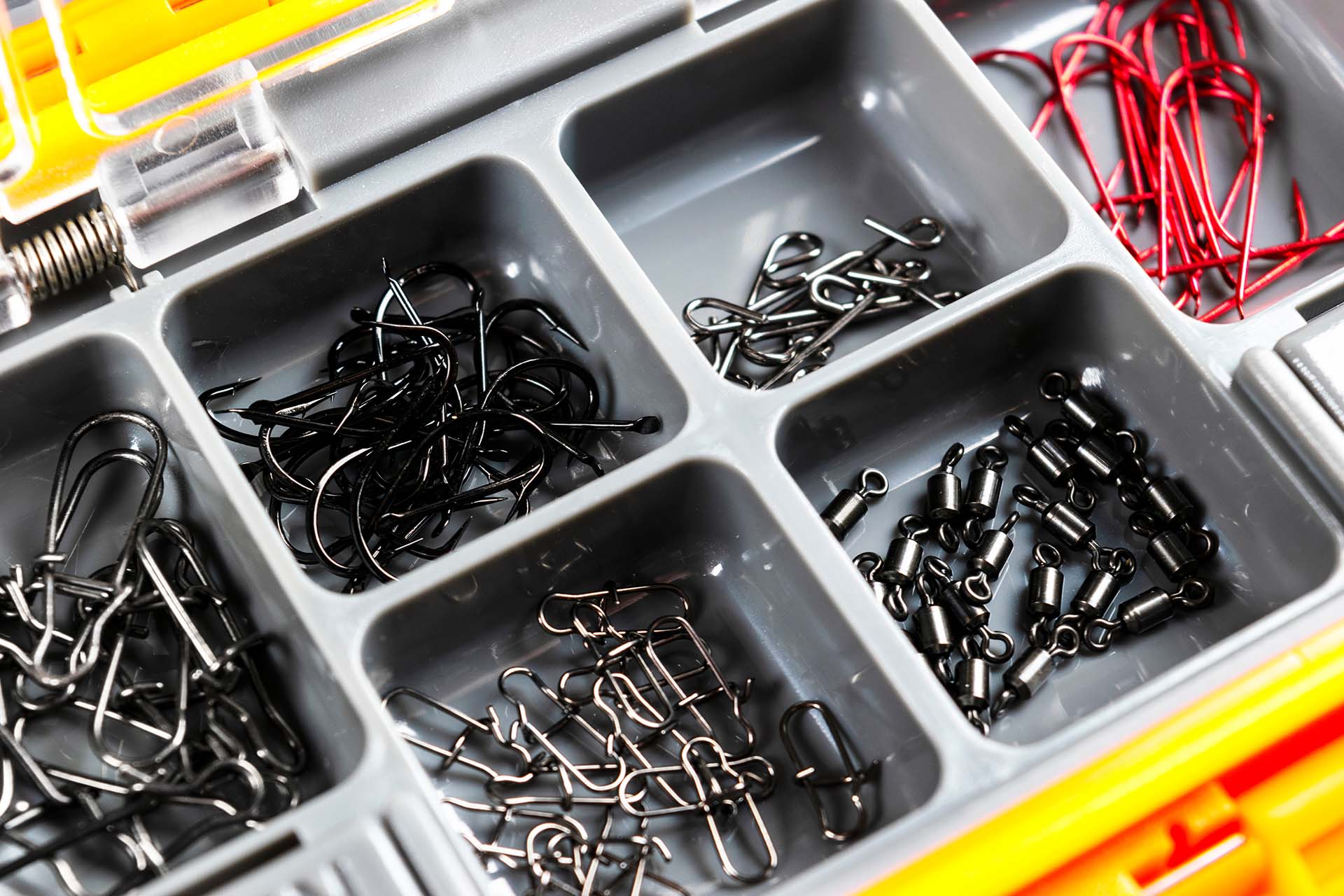 Opened tackle box with fishing hooks and accessories. Fishing hooks in box sections. Case for tackle elements. Fishing accessories background close-up.
