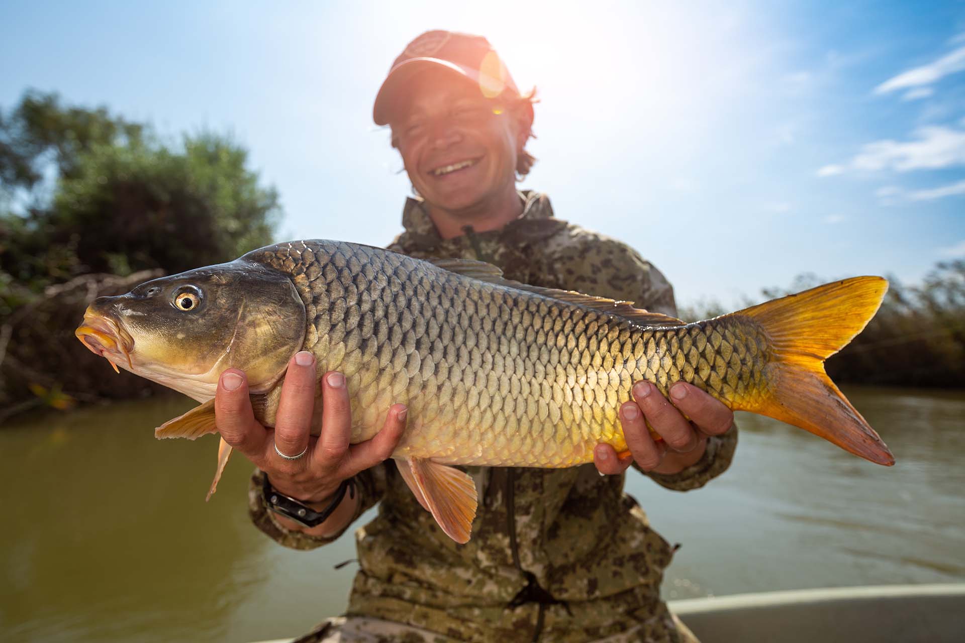 Happy angler holds big carp fish (Cyprinus carpio) and smiles. Astrakhan region, Russia