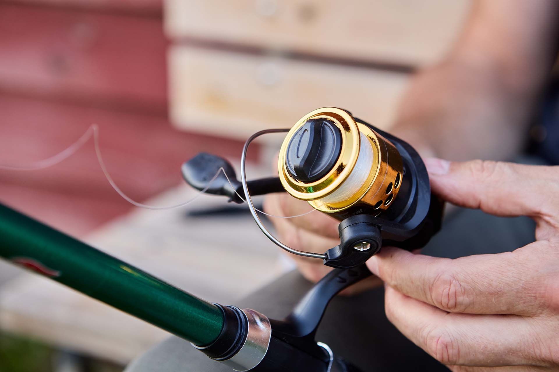 Spinning fishing reel is mounted on rod, fisherman winds line on bobbin.