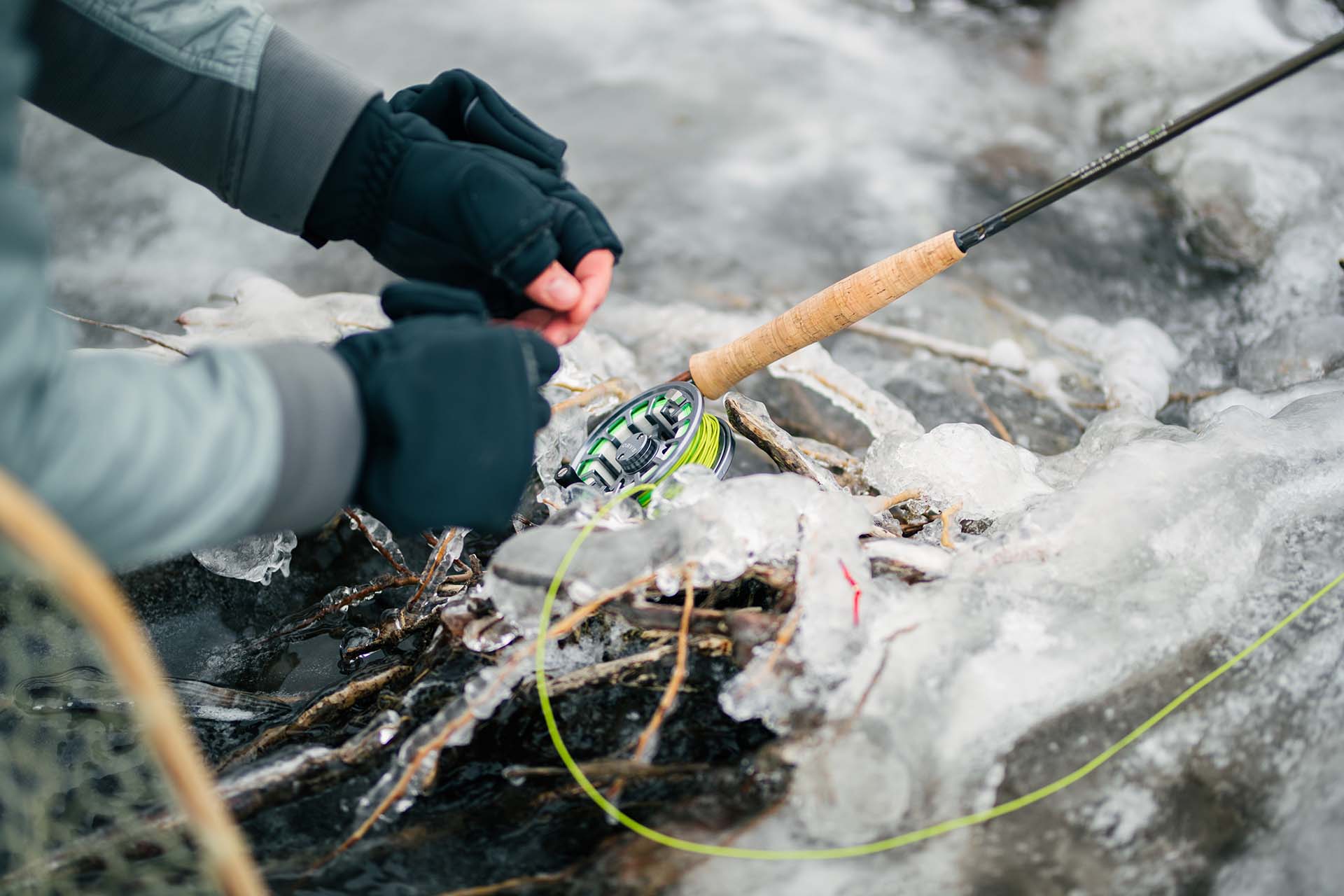 Person with gloves and a brown and black fishing rod in ice