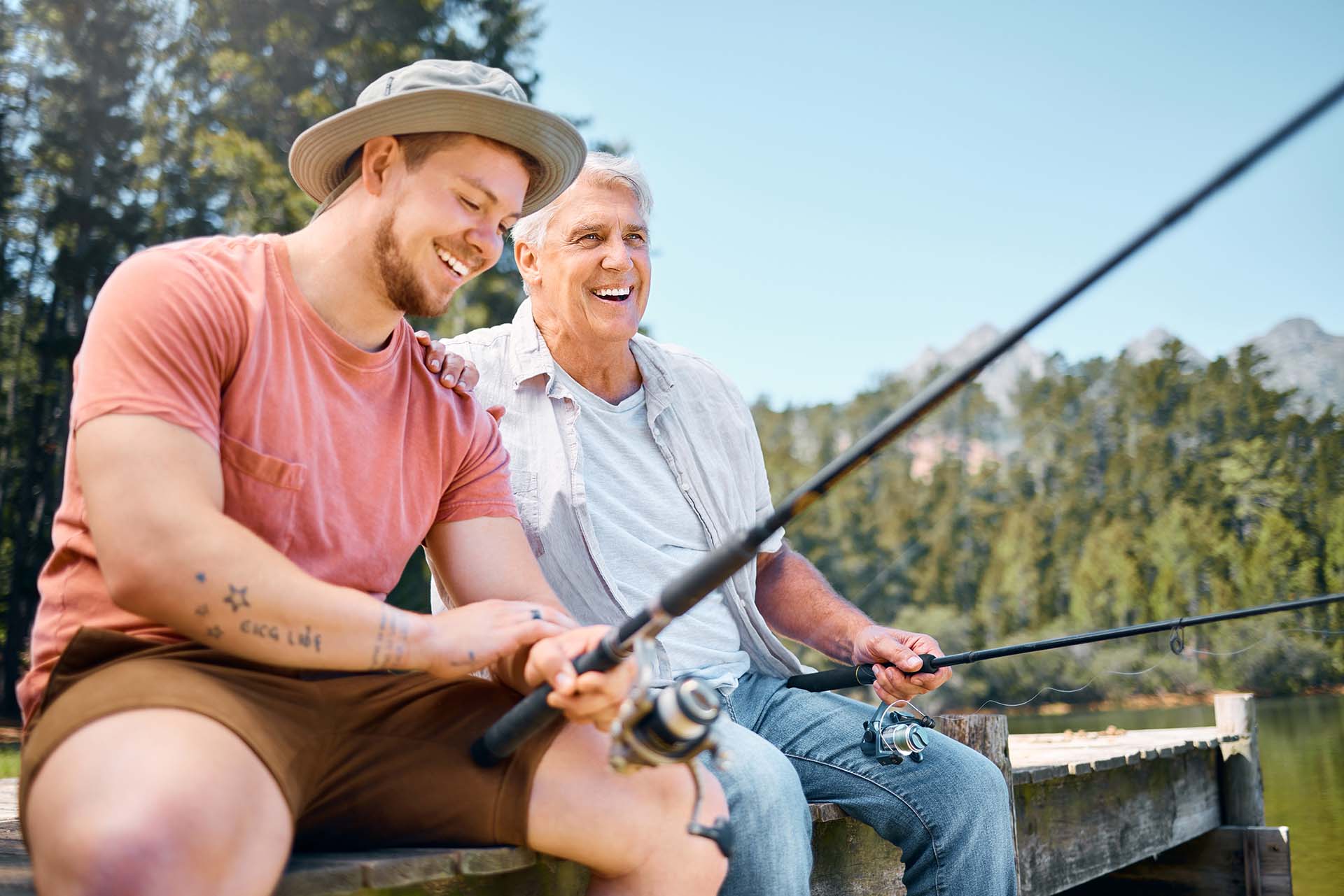 Happy man, father and fishing in lake for fun bonding, hobby or relaxing together in the nature outdoors. Elderly male person laughing with son and enjoying time to catch fish on holiday by forest.