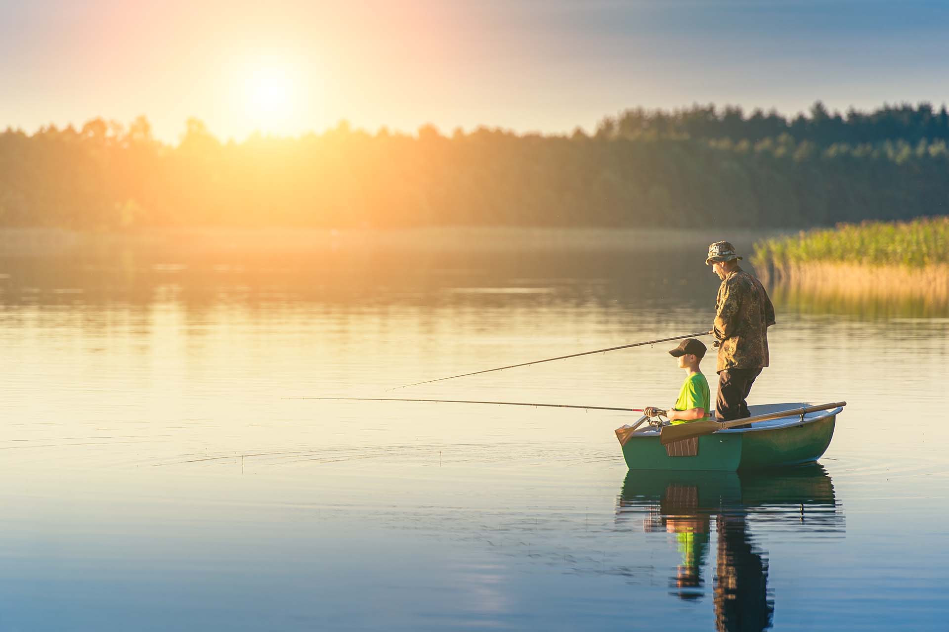 father and son catch fish from a boat at sunset