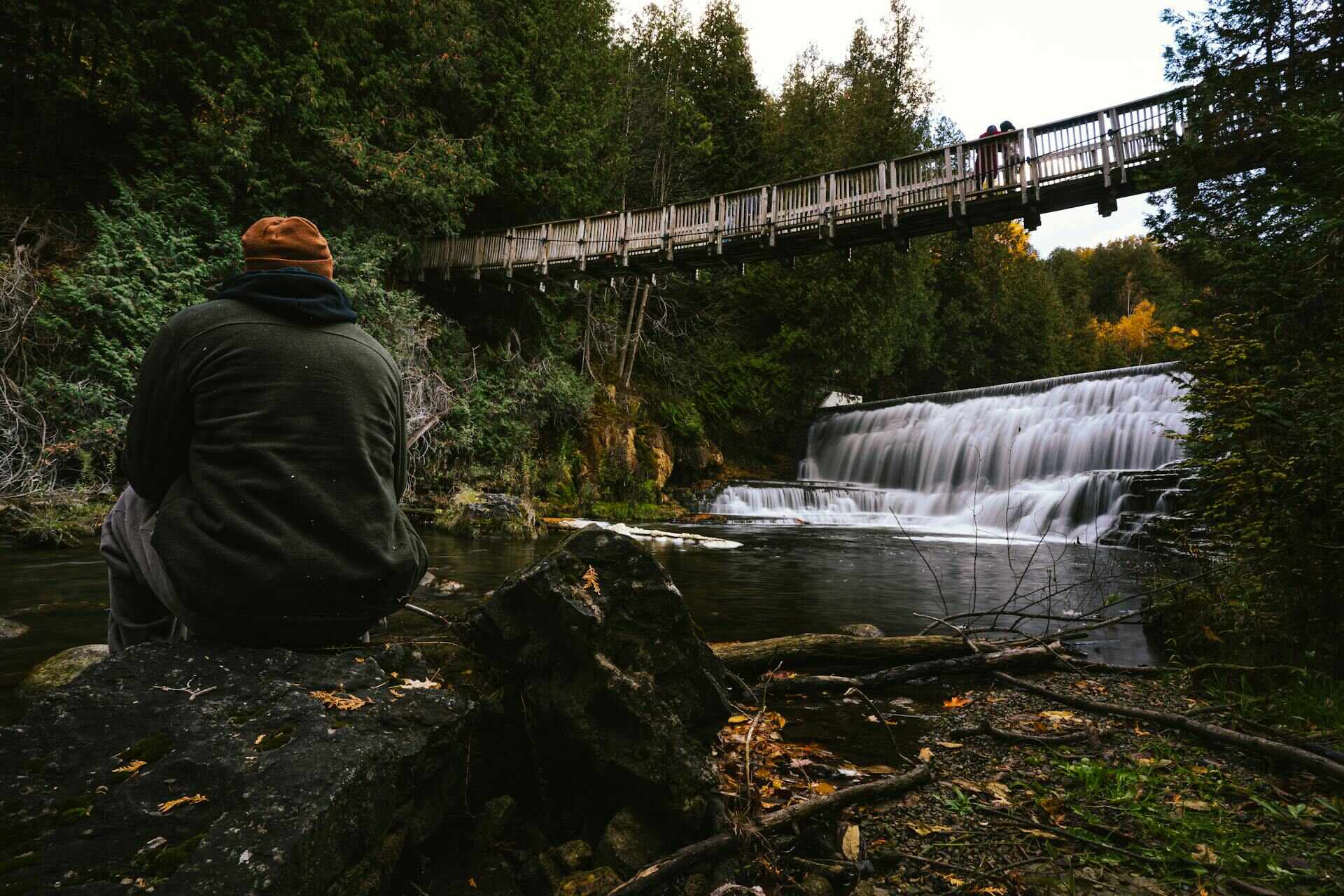 A man in a beanie sitting on the river bank